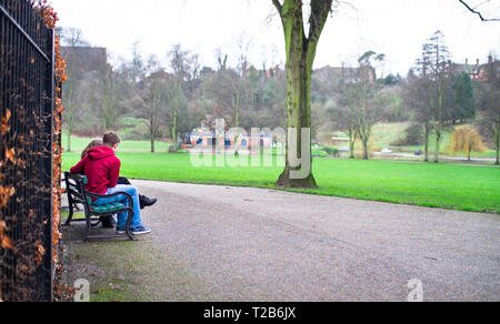 A young couple sits on a park bench in Shrewsbury, Shropshire, England. Stock Photo