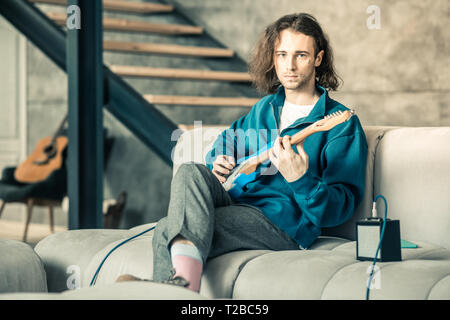 Handsome extraordinary man wearing stylish outfit while training his guitar skills Stock Photo
