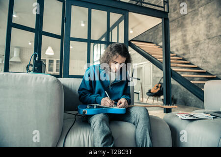 Focused dark-haired guy writing down notes in special album Stock Photo