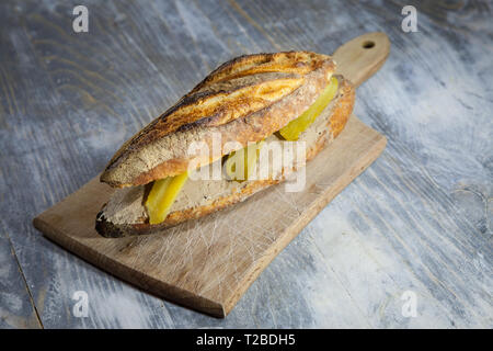 Liver Pate sanwdich in a French baguette, made of duck and chicken Pate de Foie with some sliced pickles, on display on a rustic wooden table. It is a Stock Photo
