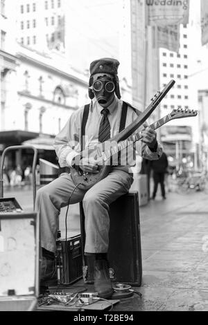 Street busker playing a guitar with a gas mask on. Stock Photo