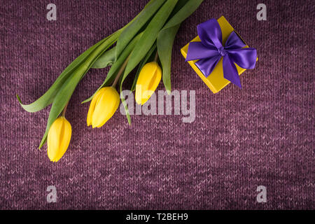 Yellow tulips and gift box on violet knitted background Stock Photo