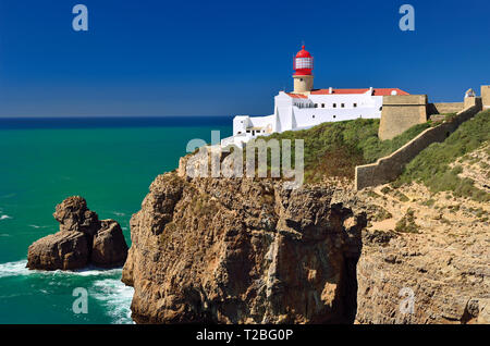 Red lighthouse with white building on a rocky cliff on a sunny day with blue sky and green ocean water Stock Photo