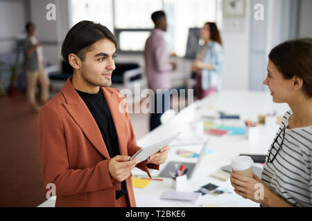 Waist up portrait of young Middle-Eastern businessman talking to colleague standing in modern office, copy space Stock Photo