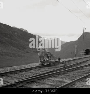 1950s, historical, railway worker standing on a railway track with a draisine or what is also called a railbike, a  special bicycle adapted for use on railway tracks, Norway. This light auxillary rail vehicle is used by service personnel to transport crew and and materila necessary for the maintenance of the railway infrastructure. This draisine looks like it has a small petrol engine attached to its frame. Stock Photo