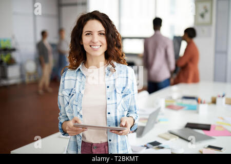Waist up portrait of contemporary woman posing at workplace and smiling at camera, copy space Stock Photo