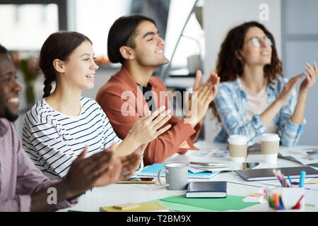 Group of young people clapping sitting in row during presentation in modern office, copy space Stock Photo