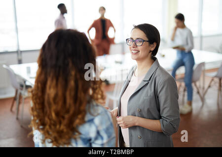 Waist up portrait of young female professional smiling happily while talking to colleague in modern office, copy space Stock Photo