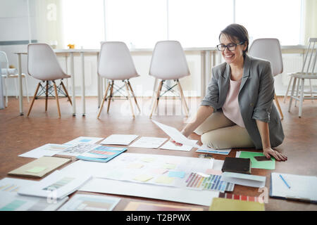 Full length portrait of smiling businesswoman sitting on floor in office while planning project , copy space Stock Photo