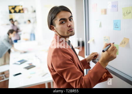 Waist up portrait of contemporary Middle-Eastern businessman drawing on whiteboard in office and looking at camera, copy space Stock Photo