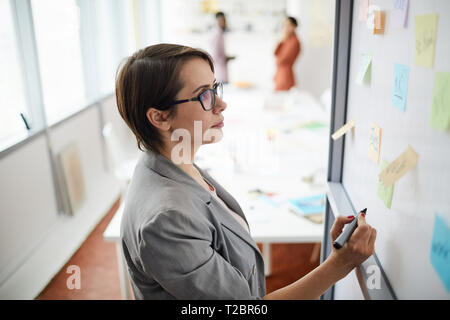 High angle portrait of contemporary businesswoman writing on whiteboard in office and thinking, copy space Stock Photo