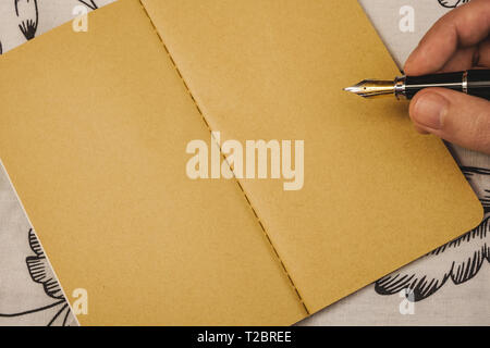 Male hand writing with fountain pen on kraft paper notebook. Special event or occasion with copy space. Stock Photo