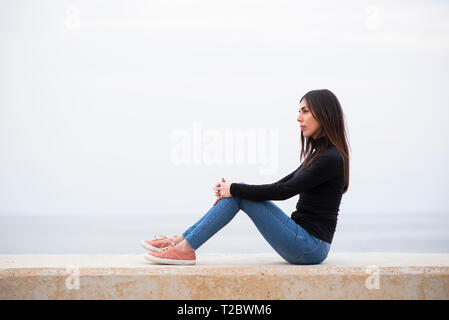 Side view of a young woman sat on the beach Stock Photo