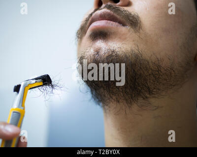 closeup man use yellow shaver shaving messy beard and mustache on his face in bathroom Stock Photo