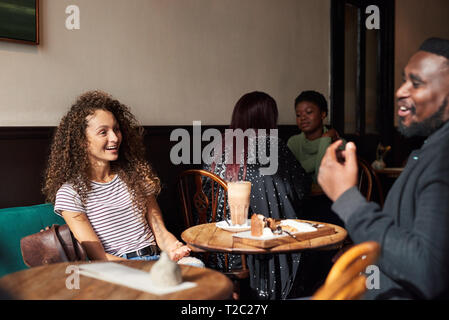 Two young friends laughing while drinking coffee and talking together in a trendy cafe Stock Photo