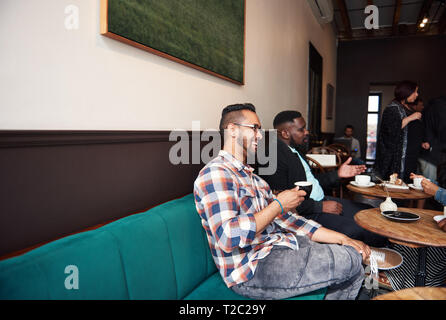 Two young men sitting at a table in a trendy cafe drinking coffee and laughing while hanging out with friends Stock Photo