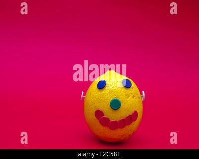 A happy face made with a lemon and colorful pins. Isolated on magenta background. Stock Photo