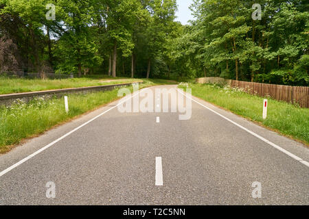 Empty two lane road leads through a green landscape in summer Stock Photo