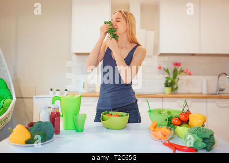 Vegan beautiful blonde woman enjoys the smell of organic parsley before cooking in kitchen. Vegetarian food. Healthy food. Vegan diet Stock Photo