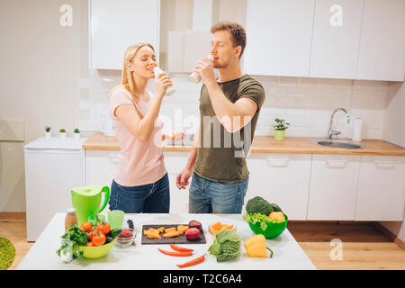 Vegan young loving family drinks natural smoothie while cooking raw vegetables in the kitchen. Diet detox. Happy couple. Raw food diet. Vegetarian Stock Photo