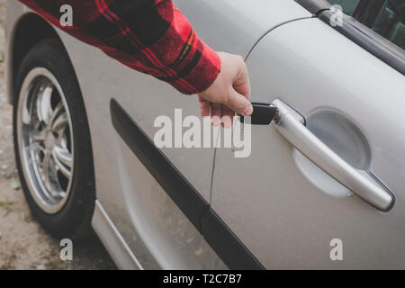 Closeup of a man's hand inserting a key into the door lock of a car. Unrecognizable white man opens vehicle door by key. Casually dressed man locks or Stock Photo