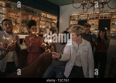 Group of young friends laughing and celebrating with sparklers while hanging out together in a trendy bar Stock Photo