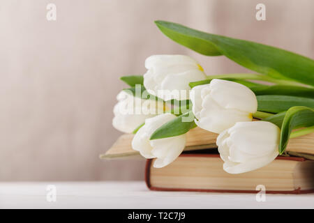Beautiful composition with white tulips and old books on a beige blurred background in the morning light. Spring reading. Stock Photo