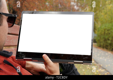 Close-up of casual dressed young man using modern digital tablet while sitting atpark, sun light. Blank white monitor screen. young guy lies in Park o Stock Photo