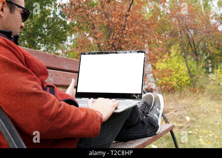 Close up man sitting in the park and using laptop computer. Blank screen for design. Free man traveler with ultrabook on the bench looking at the moni Stock Photo