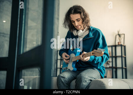 Peaceful good-looking guy with tattoo on the face playing on guitar Stock Photo