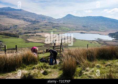 Two female hikers stopping to take off layers getting too warm on a hike up Y Garn on the Nantlle Ridge above Rhyd Ddu, Gwynedd, Wales, UK, Britain Stock Photo