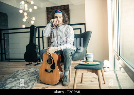 Melancholic handsome musician showing acoustic guitar while holding it Stock Photo
