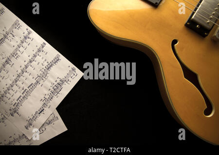 Vintage archtop guitar in natural maple close-up from above with musci sheets on black background Stock Photo