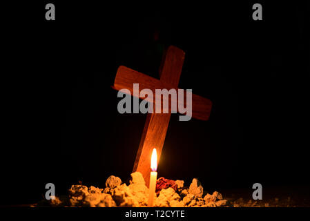 Burning candle under Jesus cross in a cemetery against black background. Stock Photo