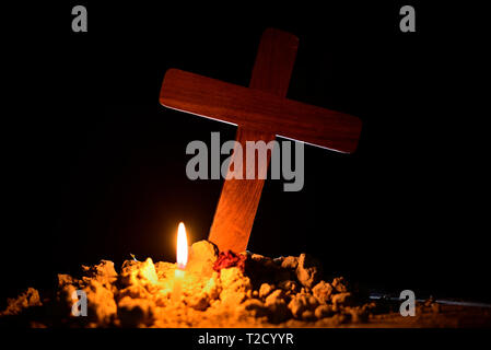 Burning candle under Jesus cross in a cemetery against black background. Stock Photo