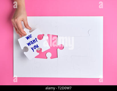 hand holding a white puzzle with the words we want you, pink background, staff recruitment Stock Photo