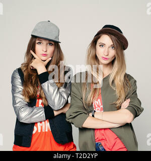 Portrait of two best friends hipster girls wearing stylish bright outfit, hats and pink lips, folded hands across on the chest. Posing on white studio Stock Photo