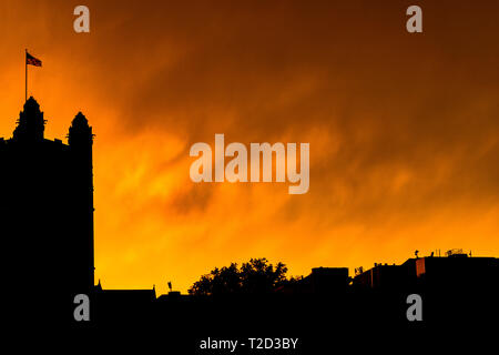 Silhouette of Harlem skyline with the American flag waving in the wind, against a bright yellow fiery-looking sky during sunset, Harlem, New York City Stock Photo
