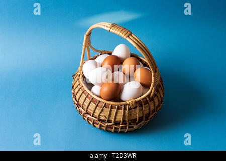 White and blue eggs in a basket over blue background, front view, horizontal image. Stock Photo