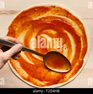 Chef adding sauce, spreading tomato paste on pizza base, top view, crop Stock Photo