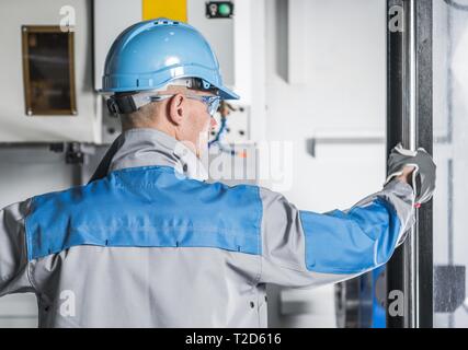 CNC Machinery Technician. Caucasian Metalworking Worker in His 30s in Front of Computer Numerical Controlled Machine. Stock Photo