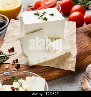 Block of feta cheese, herbs and spicies on wooden board over concrete background. Greek cuisine concept Stock Photo