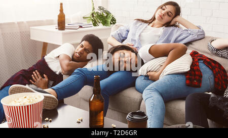 Hangover after party. Friends suffering from stomachache lying on sofa in messy room Stock Photo