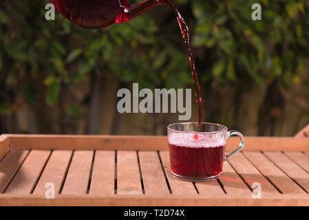 Pouring fruit tea from teapot into a cup, natural background Stock Photo