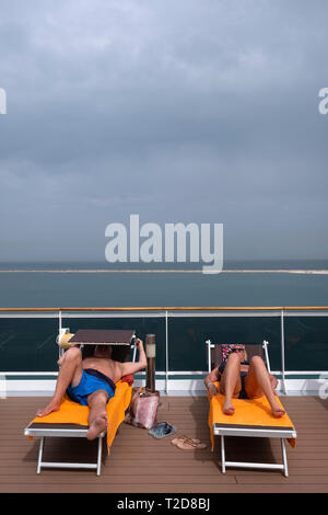 Two people sunbathing on the deck of a cruise ship Stock Photo