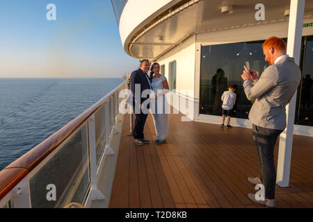 Man taking pictures of a bride and groom with his smartphone while on the deck of a cruise liner ship Stock Photo