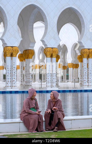Two women talking in front of the Sheikh Zayed Grand Mosque, Abu Dhabi, United Arab Emirates Stock Photo