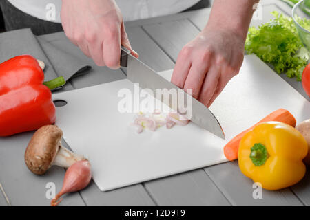 Chef slicing an onion with a santoku knife. Man cutting vegetables on a white board. Cooking at restaurant kitchen. Stock Photo