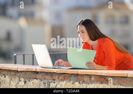 Entrepreneur works comparing documents online with a laptop in a balcony Stock Photo