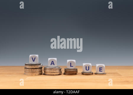 Symbol for decreasing value. Dice placed on stacks of coins form the word 'value'. Stock Photo